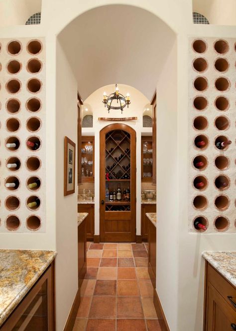 An elegant archway is flanked by built-in stone wine racks that hold the homeowners' collection. Warm wood cabinets paired with traditional countertops provide storage for glasses, decanters and other entertaining needs. Terracotta tile grounds the space, while a rustic chandelier adds an Old World note. Hacienda Architecture, Mediterranean Wine, Spanish Home Interior, Spanish Homes, Wine Rooms, Spanish Mediterranean, Home Wine Cellars, Basement Inspiration, Big Room