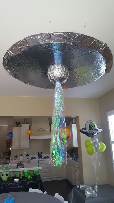 UFO / alien spaceship decoration made from foam board, duct tape, spray adhesive, tin foil, Styrofoam ball, battery operated strobe light, cellophane. hung with command hooks and fishing line. Savory Space Themed Food, Spaceship Decorations Diy, Alien Spaceship Decoration, Spaceship Party Space Theme, Alien Themed Decorations, Diy Alien Decor, Spaceship Theme Party, Sci Fi Birthday Party, Aliens Birthday Party