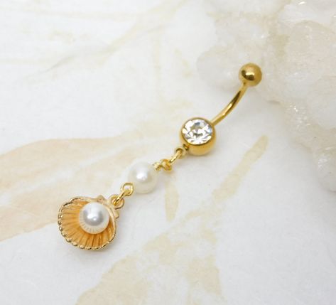 Seashell Pearl Dangle Belly Ring Show off your beautiful belly! Belly ring features a beautiful golden shell charm with faux pearl inside charm accented with a white freshwater pearl.  Belly button ring measures 2 1/4 inches long total length. Barbell is 14g gold-plated surgical steel with a 7/16" (11mm) wearable bar length. For Belly Button Rings: https://www.etsy.com/shop/AllAboutClass?section_id=18474235&ref=shopsection_leftnav_1  All body jewelry sales are final!!  AllAboutClass DOES NOT acc Belly Button Rings Dangle, Gold Belly Button Rings, Belly Button Piercing Jewelry, Dangle Belly Rings, Jewelry Tattoo, Belly Piercing, Belly Button Ring, Belly Button Piercing, Dope Jewelry