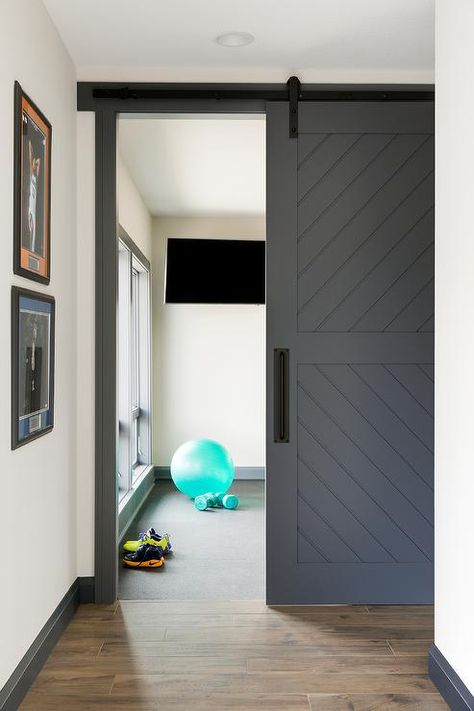 A dark gray plank barn door on rails is accented with a matte black handle and opens to a home gym boasting a flat panel television. Basement Home Gym, Basement Gym Ideas, Rustic Basement, Basement Gym, Black Barn, Home Gym Design, Gym Decor, Sliding Doors Interior, Interior Barn Doors