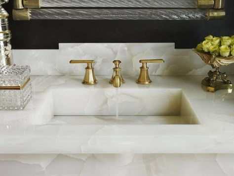 A white onyx vanity top is fitted with a brass faucet kit sat in front of an onyx backsplash and below a glass and brass vanity framed by black walls. Onyx Bathroom Ideas, Onyx Countertops, Custom Sinks, White Onyx, Vanity Countertop, Sink Countertop, Brass Faucet, Bathroom Countertops, White Rooms