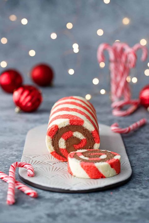 Red and white striped cake roll with one slice cut off to show a perfect spiral of chocolate peppermint whipped cream filling, with candy canes, red ornaments, and Christmas lights out of focus in the background. Peppermint Roll, Christmas Cake Roll, Candy Cane Cake, Peppermint Whipped Cream, Xmas Baking, Striped Cake, Cake Roll Recipes, Log Cake, Festive Food