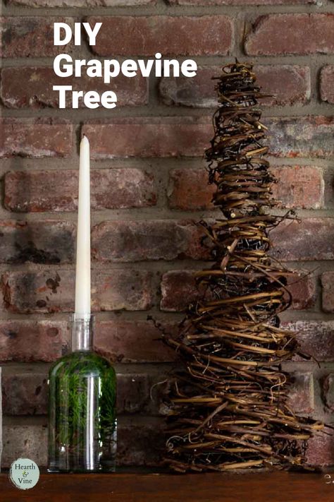 A cone shaped tree made from grapevines sits on a mantle with a bottle and candle. Things To Make With Grape Vines, Hanging Grapevine Wreath From Ceiling, Grapevine Craft Ideas, Grapevine Christmas Trees, Grapevine Garland Front Door Christmas, Grapevine Swag Ideas, Diy Grapevine Tree, Grapevine Crafts Diy, Grape Vine Christmas Tree