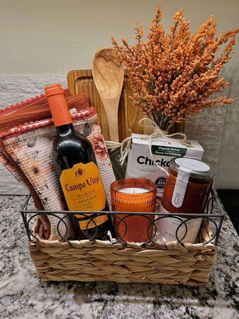 Fall themed gift basket with orange and wood accents. Gift basket is pasta date-night themed and includes red Italian wine, gluten free chickpea pasta, pasta sauce, candle, kitchen towel, wooden spoon and orange accents. Accents are decorative floral and tweed. Pasta Night Gift Basket, Wine And Pasta Gift Basket Ideas, Date Night Hamper, Pasta Making Gift Basket, Pasta Themed Gift Basket, Kitchen Basket Gift Ideas, Italian Basket Gift Ideas, Charcuterie Basket Ideas, House Warming Basket Diy