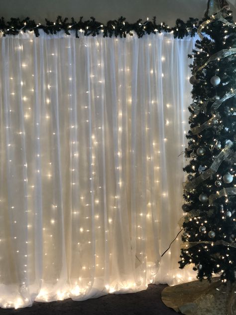 Christmas Backdrop (Pipe and Drape with string lights and greenery. Christmas Drapes Ideas, Christmas Photography Backdrops Diy, Winter Theme Backdrop, Simple Christmas Backdrops For Photos, Winter Party Backdrop, Christmas Pictures Backdrop, Christmas Wedding Photo Backdrop, Simple Christmas Photo Backdrop, Christmas Photobooth Backdrop