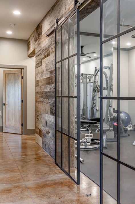 Whatever kind of room you want in your home, we'll design it! We love these glass barn doors leading into this client's awesome home gym. This room is where functional meets modern, and we are obsessed! ID.ology Interiors & Design can make all of your home dreams come true. We are based out of (but not limited to) Asheville, NC. Check out our website to learn more! Glass Gym Room, Basement Gym Door Ideas, Gym With Glass Doors, Glass Wall Gym Design, Basement Gym Glass Walls, Rustic Workout Room, Basement Gym Glass Door, Modern Home Gym Interior Design, Basement Gym Doors