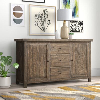 This farmhouse 67'' sideboard doubles as a serving station in your dining room or a TV stand in your living room. Crafted from solid wood, it features a rectangular silhouette balanced on low feet. A rustic wood finish and window-pane paneling add a barn-inspired touch that we love in any antiqued aesthetic. Plus, it offers plenty of storage: Two cabinet doors open up to four shelves that are just right for books or decor, while three drawers let you tuck away tech accessories, utensils, or extr Modern Storage Cabinet Living Room, Buffet And Sideboards, Modern Farmhouse Sideboard, Acacia Wood Sideboard, Kitchen Buffet Cabinet, Serving Station, Diy Farmhouse Ideas, Rustic Sideboard, Modern Storage Cabinet