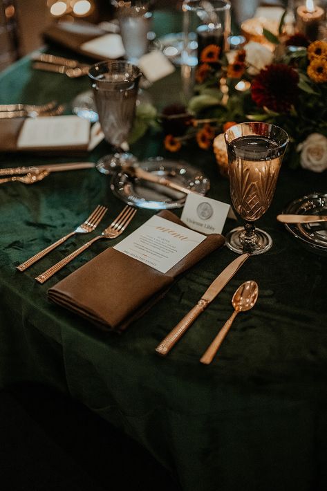 Round tables with dark green velvet and brown napkins with copper flatware make up this moody fall wedding reception table. Copper And Green Table Setting, Wedding Brown And Green, Copper Green Black Wedding, Wedding Decor Forest Green, Green Gold And Brown Wedding, Emerald Wedding Colors Decor, Fall Wedding With Green, Copper And Forest Green Wedding, Green And Brown Wedding Decor