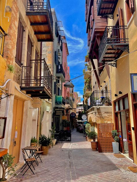 A picture of a beautiful, colorful hidden side-street in Chania, Crete, Greece. The street is empty, the buildings are colorful and has balconies. The sky in-between the buildings are perfect blue Crete Greece, Hidden Gem, Crete, Greece