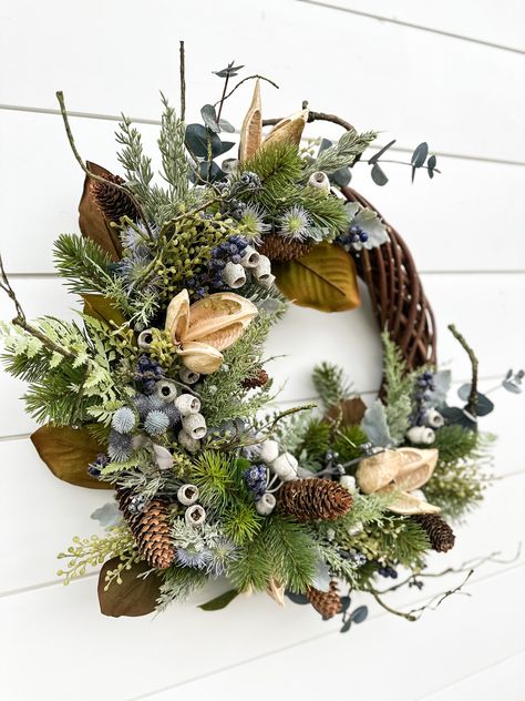 This wreath features a variety of different pine and evergreen artificial stems. It has accents of navy blue berries, twisty vines, and green forest artificial accents. This design is topped with my favorite weather sage naturals:  pine cones, navy Gum Berries, and ivory bell pods. The florals are carefully woven by hand into this sturdy 18" willow wreath base. From the end of the last floral on the left to the wreath base on the right, the design measures 22".  This wreath would look beautiful Unique Wreath Ideas, January Wreath Ideas, January Wreath, Favorite Weather, Farmhouse Wreaths, Twig Crafts, Floral Antlers, Bird Wreath, Willow Wreath