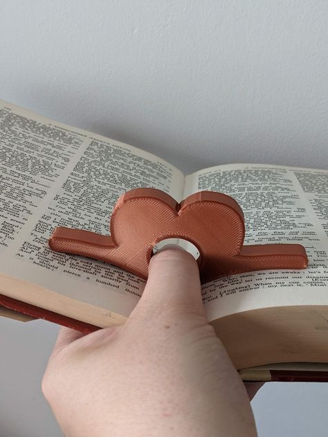 This cute heart-shaped book page holder is 3D printed and is an incredibly useful reading aid that helps you hold your book open with ease using only one hand! It's ergonomically designed to spread the pages of your book and it sits in such a way as to take some of the weight and pressure off your thumbs while reading. They'd also make fantastic gifts for the book lovers in your life. Each book page spreader is made to order, so you can choose from my large selection of colours. I can also perso Book Page Holders, Clay Page Holder, Ceramic Book Holder, Clay Book Holder, Clay Bookends, Ceramic Book Ends, Hand Reading, Ceramic Book, Book Page Holder