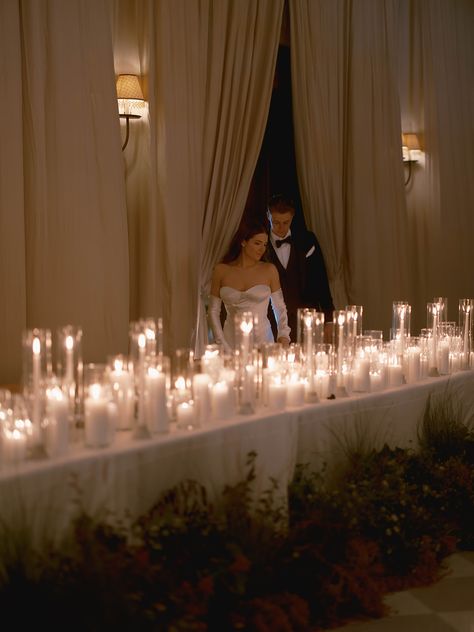 This wedding reception head table was covered in pillar candles and lined with organic florals. The bride and groom were seated with their nearest and dearest bridal party members. The draped ballroom made for the most stunning moody wedding. Candle Bridal Table, Romantic Candle Light Wedding, Bridal Table Candles, Candles And Lights Wedding, Head Table Candle Decor, Candlelit Sweetheart Table, Bride And Groom Dinner Table, Head Table With Bridal Party, Hotel Ballroom Wedding Receptions