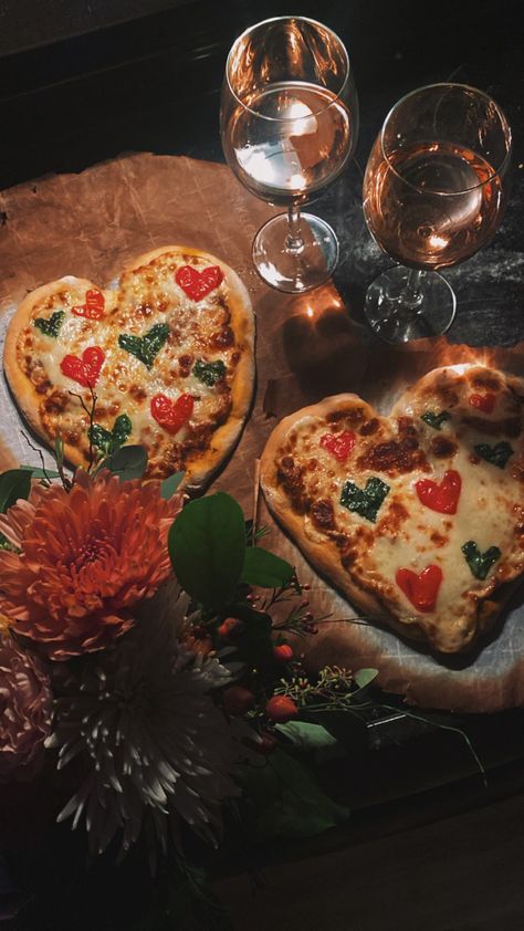 two heart shaped pizzas with heart shaped basil and tomatoes on top. two glasses of wine line the top of the photo and flowers peek in from the bottom. Homemade Pizza Valentines Day, Heart Shaped Pizza Valentines, Love Dinner Romantic, Heart Pizza Valentines, Heart Shaped Margarita Pizza, Homemade Heart Shaped Pizza, Valentines Aesthetic Pictures, Valentine Vibes Aesthetic, Surprises Aesthetic