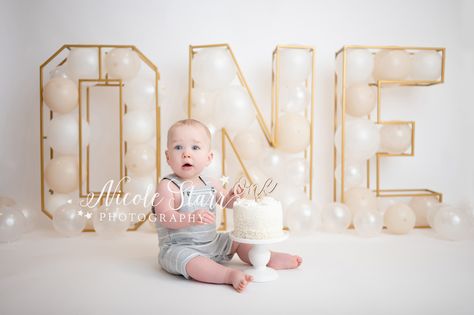 baby boy sits in grey and white overalls with gold ONE behind him filled with balloons and white birthday cake with wooden ne topper for cake smash with Saratoga Springs cake smash photographer Nicole Starr Photography Neutral Cake Smash, All White Cake Smash Photoshoot, All White Smash Cake Photos, Star Cake Smash, White Balloon Cake Smash, Pastel Cake Smash, Neutral Cake, Topper For Cake, First Birthday Theme Boy