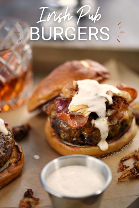 a beef patty on a pretzel bun topped with melted cheese, bacon slices, caramelized onions and sauce dripping down the sides with a metal ramekin of sauce and glass of whiskey in the background. Irish Lunch, Pub Burger Recipe, Pub Burgers, Irish Pub Food, Delicious Burger Recipes, Irish Dinner, Irish Cooking, Hp Sauce, Irish Cuisine