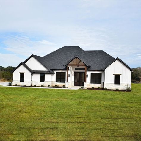 White farmhouse exterior with white vertical siding, black windows, black roof, white rock exterior, cedar trellis and cedar details White Ranch Black Windows Exterior, Black Tile Roof White House, White Siding Black Roof Farmhouse, White And Black Farmhouse Exterior Ranch, Modern Home Black And White Exterior, White Brick House Farmhouse, White House Vertical Siding, White Brick Black Roof House, Black And White House Exterior With Stone