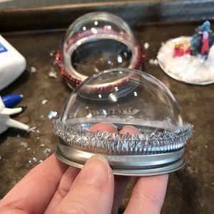 Mason Jar Snow Globe Toppers – TheRoomMom Snow Globe Mason Jar, Mason Jar Snow Globe, Mason Jar Lids Ornaments, Christmas Mason Jars Diy, Christmas Treats For Gifts, Clear Plastic Ornaments, Christmas Treats Holders, Jars Snow, Globe Crafts