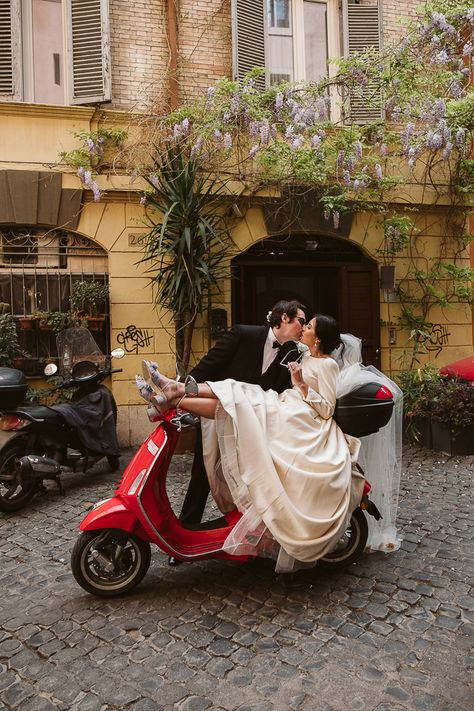 Bride and groom kiss while riding on a cute, red scooter l Image by Blancorazon Wedding