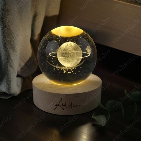 This enchanting night light features a meticulously detailed moon design, bringing the serene beauty of the night sky into your home. The sphere, measuring 2.4 x 2.4 inches, is crafted with precision to capture the intricate details of the lunar surface. - Ball Size: 2.4 * 2.4" - Round Wooden Base: 2.7 * 2.7" - The wooden base can be engraved. Just select the font in the drop-down box. - Requires plugging in to illuminate. Home Decor: Enhance your living space with a unique and elegant night lam Planet Room Decor, Planet Room, Moon Night Light, Lunar Surface, Lamp 3d, Loft Furniture, Astronomy Gift, Moon Lamp, Light Crystal