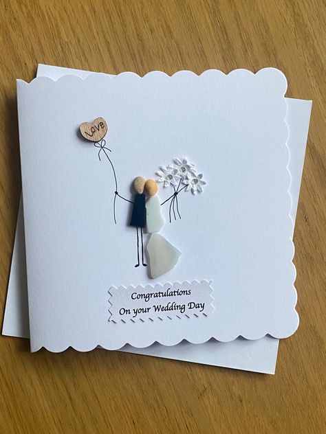 "Handmade Wedding Day Card  Decorated with coloured glass, paper flowers and wooden heart Give the marrying couple a beautiful and unique pebble card to treasure forever Measures 5 x 5\" (12.7 x 12.7cm) and comes with a white envelope Blank inside so you can write your own personal message Message text on tag can be changed to a more personalised one of your choice This card is made to order and although I always try to make others as close as possible to the one pictured here, this is not always possible due to the variation of the pebbles in size, shape and colour." Congrats Wedding Cards Handmade, Simple Wedding Cards Handmade, Handmade Wedding Cards Ideas Beautiful, Wedding Day Cards Handmade, Wedding Cards Handmade Congratulations, Diy Wedding Cards Handmade, Handmade Wedding Cards Ideas, Unique Wedding Card Design, Pebble Cards