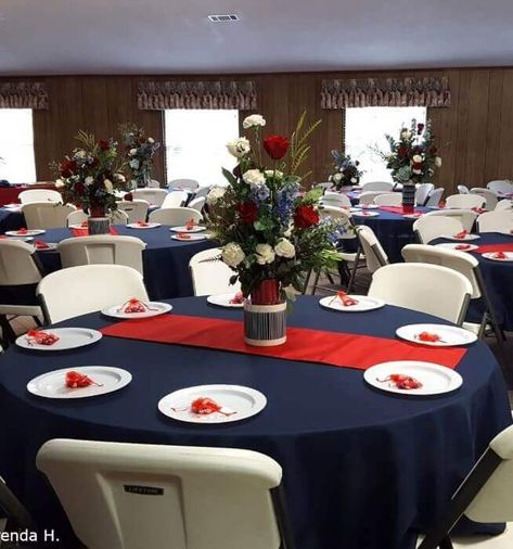 Set a dazzling tablescape by incorporating a classic red and blue color combination into your décor. Drape the table with a navy blue tablecloth and spread a red table runner on top for a fascinating allure. Exquisitely arrange white & red roses along with foliage in a unique vase to impart a majestic charm. Place white plates along with red rose stems to exude an enthralling appeal elevating your event decor to the next level. Patriotic Table Decor, Runner Wedding Table, Blue Graduation Party, Satin Table Runner, Wedding Reception Layout, Navy Table, Pipe And Drape Backdrop, Wedding Table Runner, Red Wedding Decorations