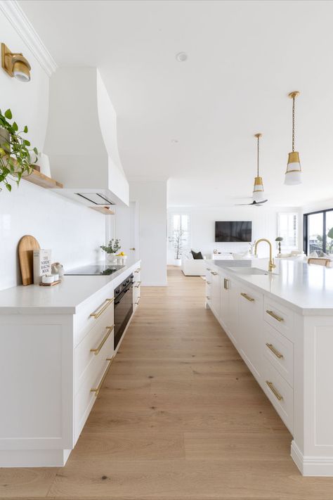 The hamptons style kitchen features blonde oak flooring, white Shaker cabinets, and brushed brass tapware.