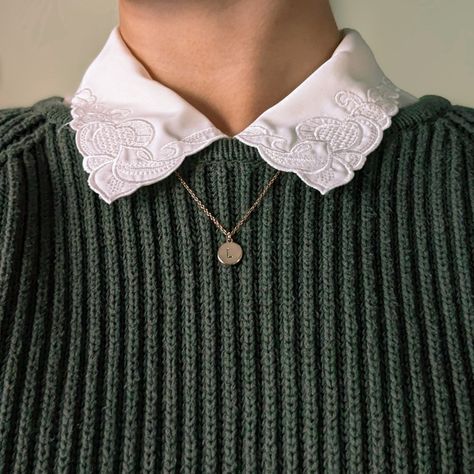 This photo shows the area of a body below the chin and just above the chest. It's zoomed in to show the texture on the dark green, cable-knit sweater worn over a cream-colored button down with swirly embroidery on the collar. Underneath the collar there is a dainty gold chain that hangs down with a gold circle stamped with the letter 'L'. This image is an emphasis on cozy textures. Collar Over Sweater, Sweater Collared Shirt Outfit, Collared Shirt With Sweater, Collard Shirt Under Sweater, Collar Under Shirt, Collar Shirt Under Sweater, Collared Sweater Outfit, Sweater With Collared Shirt, Sweaters With Collared Shirts