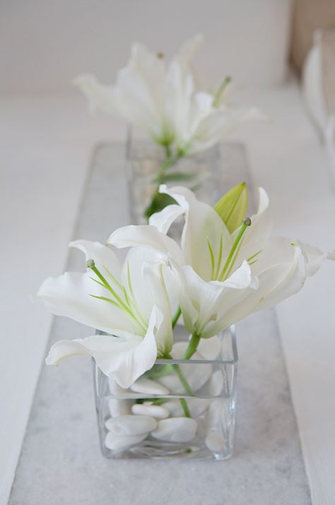 A glass container holding a couple of white lilies and white stones makes for elegant and minimal decor. Lily Centerpieces, Tafel Decor, Wedding Floral Centerpieces, Spring Wedding Flowers, Gold Anniversary, Flower Arranging, Deco Floral, White Lilies, Wedding Table Centerpieces