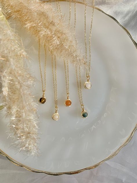 five necklaces lay on a white dish under pompous grass stems. the necklaces are all different colors and consist of a round stone hand-wrapped in a thin gold wire. the stones are tiger's eye, vanilla jade, orange aventurine, moss agate, and white quartz. the pendents are clipped onto a dainty gold chain. Wrapped Stone Necklace, Easy Necklace, January Birthstone Jewelry, Clear Quartz Necklace, Healing Stones Jewelry, Bead Charms Diy, Wire Wrapping Stones, Rose Quartz Heart, Crystal Necklaces