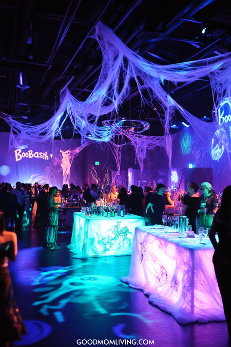 A vibrant party scene featuring colorful lighting and spooky decorations, including spider webs, with guests socializing around illuminated tables. 60th Birthday Halloween Theme, Halloween Birthday Decoration Ideas, Prom Night Halloween Party, Spooky Halloween Birthday Party, Huge Halloween Party, Middle School Halloween Dance Decorations, Halloween Party Room Decor, Spooky Pool Party, Spooky Party Decor