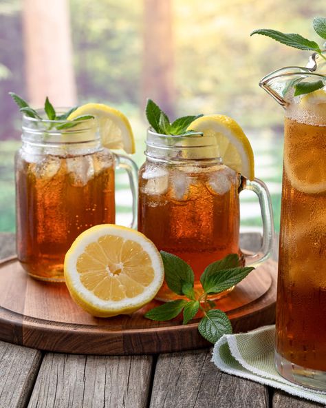 Pitcher of cold iced tea with mint, lemon slices and ice with two glasses ot tea on a wooden table and rural summer background Iced Tea Aesthetic, Ice Lemon Tea, Iced Tea Maker, Tea Aesthetic, Lemon Slices, Simply Filling, Tea Maker, Mint Tea, Glass Carafe