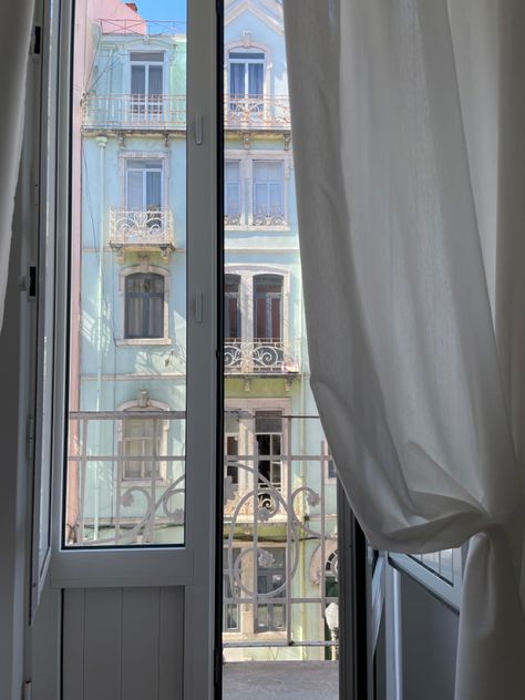 A sunny day reflecting on the colorful building walls and shining into bedroom window that’s slightly blocked by white curtain swooped to the side with the help of the balcony door/window. Lisbon Balcony, Portugal Apartment, Lisbon Aesthetic, Lisbon Apartment, Wolf Alice, Balcony Window, Sun Shining, Apartment Aesthetic, Apartment Balcony