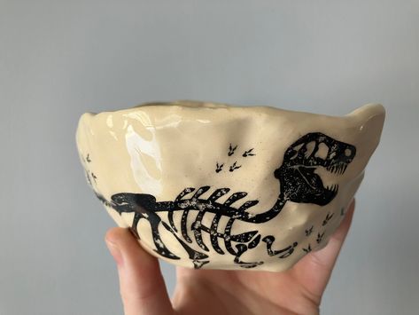 "I handbuilt this lumpy ceramic bowl using the pinch pot technique from a big ball of clay. After the bisque firing I added these dinosaur underglaze decals, clear glazed the piece, then put it back in the kiln for the final firing. Perfect for the paleontologist or dinosaur enthusiast!  The bowl holds 9oz of liquid if you're going to use it for a small cereal bowl, though at the full 9oz a child might spill the milk if not careful.  It measures roughly 2\" tall at its shortest point and 2.5\" at its tallest. It is roughly 5\" across. Microwave and dishwasher safe. Signed with my name (Rachel) and 2023 at the bottom." Cereal Bowl Pottery, Handbuilt Pottery, Pinch Pot, Pinch Pots, Big Balls, Cereal Bowl, Dinosaur Kids, Jan 20, Ceramic Bowl