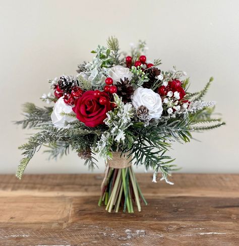 "DETAILS & SIZE  ---------------------------------------------------------- ❤ This classic  winter snow covered wedding bouquet is put together with high quality red and white silk flowers, red berries, babies breath, pinecones, eucalyptus and all sorts of different evergreens. The handle is also wrapped with twine and finished with a twine bow to give it a beautiful rustic touch. This bouquet is perfect for a wedding in winter or around Christmas. Available in 5 different sizes. The 12\" brides bouquet is photographed in the listings Before you choose the size of bouquet that you like, I would highly recommend that you measure the size against yourself to make sure that you choose the perfect size for you.  MATCHING BOUQUET: https://www.etsy.com/ca/listing/1572923381/red-wedding-bouquet-r Red White Green Wedding Flowers, Christmas Wedding Ring Bearer, Outdoor Christmas Wedding Ideas, Wedding Flowers Christmas, Bridesmaid Bouquet Christmas, Christmas Wedding Buttonholes, Christmas Wedding Centrepiece Ideas, Cheap Christmas Wedding Ideas, Christmas Bridal Bouquet Winter Bride