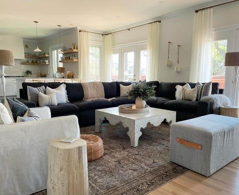 This living room features a navy blue sectional couch, a white square coffee table, and a white stuffed armchair. An unfinished tree stump end table rests on a brown oriental-style area rug next to a white-upholstered armchair. Navy Blue Armchair Living Room, Dark Blue Sectional Living Room, Blue White Brown Living Room, Navy Sectional Living Room, Navy Couch Living Room, White Square Coffee Table, Blue Sectional Couch, Navy Blue Sectional, Stump End Table