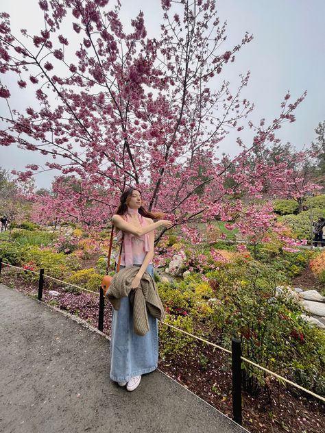 girl standing in front of Japanese cherry blossom tree wearing a spring outfit, pink top and denim skirt Japanese Garden Outfit Ideas, Cherry Blossom Fashion Outfit, Cherry Blossoms Outfit Ideas, Cherry Blossom Festival Outfit Ideas, Outfit For Cherry Blossom Season, Japan Spring Fashion Cherry Blossoms, Cherry Blossom Viewing Outfit, Japan Sakura Season Outfit, Japan Outfit Cherry Blossom