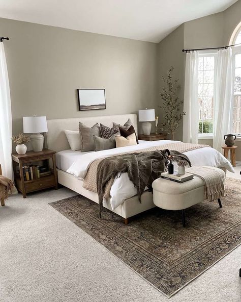 A large modern farmhouse-style bedroom is designed with plush wall-to-wall carpet in a neutral light grey color. There is an antique black and brown carpet centered under the bed for additional interest and comfort. The cream fabric bed is styled with brown and tan blankets and accent pillows, and wooden side tables feature table lamps for a cozy atmosphere...   Image: brittan_allie_home Warm Bedroom, Upholstered Panel Bed, Neutral Bedroom, Small Room Bedroom, Bedroom Carpet, My New Room, Cozy Bedroom, Bedroom Makeover, Modern Bedroom