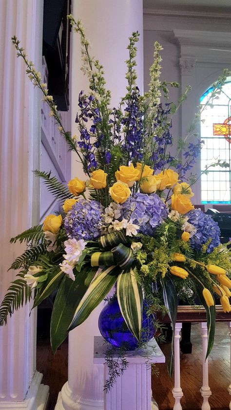 Yellow and blue theme of hydrangeas, yellow roses, yellow,tulips, white larkspur, dark blue delphiniums, lime alstromeria, sword fern, variegated aspedistra, sperengetti fern. https://www.instagram.com/p/CDNSlfQpmNW/?igshid=k5prlwi4adrm Egyptian Floral Arrangement, Blue And White Tall Floral Arrangements, Purple Blue Yellow Flower Arrangement, Easter Florals Diy Church, Blue Yellow Flower Arrangements, Podium Flower Arrangements, Blue And Yellow Flower Arrangements, Easter Flower Arrangements For Church, Cemetery Arrangements