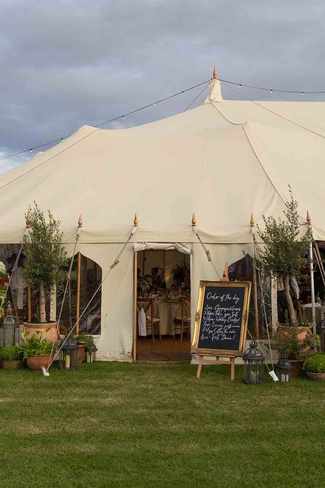 Large marquee wedding with a gold framed order of the day sign, moroccan lanterns from Onkoi and large potted plants and trees that surround the entrance of the marquee at a outdoor wedding in the Cotswolds, UK. The marquee is situated amongst a wild flower garden planted and nurtured by the bridal couple. Small Wedding Marquee, Uk Country Wedding, Wedding Flowers Marquee, Garden Marquee Party, Field Marquee Wedding, Outdoor Marquee Wedding, Backyard Wedding Marquee, Outdoor Garden Party Wedding, Wedding Marquee Flowers