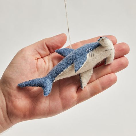 With his eyes mounted on the side of his head – our shark has 360-degree vision and can see above and below at all times! But don’t be scared - our little felt hammerhead loves to play. This adorable ornament is bound to jump from your tree and play with the kiddos. All details and stitching are hand-embroidered. Our ornaments come ready to hang with a string attached. Made from sustainably harvested merino-blended wool. Fairly traded and made with love. H: 2"/5cm W: 3.25"/8cm L: 5.5/14cm. Like Shark Felt, Shark Ornament, Felt Fish, Felting Ideas, Handmade Plushies, Hammerhead Shark, Felt Ornament, Hand Felted, Needle Felted Animals