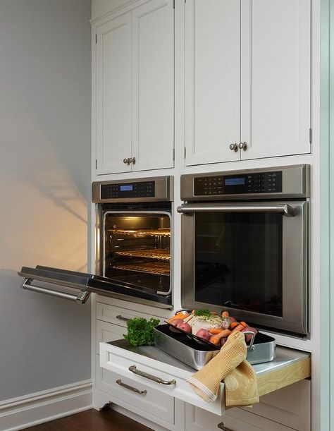 Under white shaker cabinets, side-by-side stainless steel wall ovens are mounted above pull out drawers donning polished nickel pulls and finished with pull out stainless steel countertops. Kitchen Corner Stove, Stove Wall, Corner Stove, Oven Design, Wall Ovens, White Shaker Cabinets, Transitional Kitchen, Kitchen Plans, Kitchen Remodel Idea