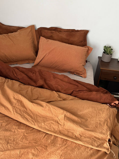 A bed with a terracotta colored duvet set and a tie dyed rust duvet set Sage Terracotta Bedding, Terracotta Yellow Bedroom, Orange Sheets Aesthetic, Mustard And Terracotta Bedroom, Bedding Color Combo Ideas, Green Bedrooms Ideas, Bedroom Ideas Terracotta, Terracotta Bedroom Decor, Green Bedroom Paint Colors