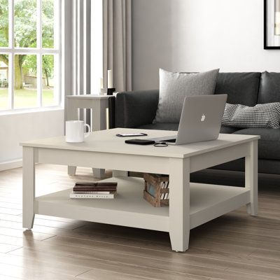 This coffee table brings classic style and neutral tones to your living space. It's made from engineered wood with a neutral finish, and it stands on four tapered legs. This coffee table has a streamlined square silhouette, blending in with nearly any living room seating area. Stack coffee table books on its exposed lower shelf, and rest a vase of flowers and tray of warm beverages on its surface. This clean-lined piece complements traditional and contemporary decor alike. Lark Manor™ Color: Ivo Stack Coffee Table, Room Seating Area, A Vase Of Flowers, Vase Of Flowers, Solid Wood Coffee Table, Room Seating, Cool Coffee Tables, Table Books, Table With Storage