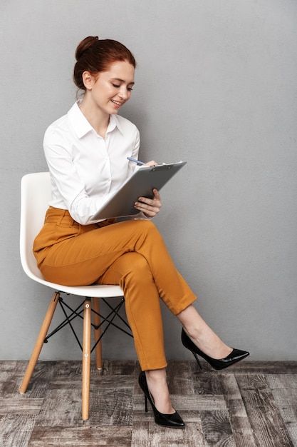 Premium Photo | Beautiful woman posing on chair Leaning Over Desk Pose Reference, Poses With A Chair, Sitting In Chair Pose, Posing On Chair, Woman Sitting In Chair, Holding Clipboard, Woman Looking Down, Sitting At Desk, Study Reference