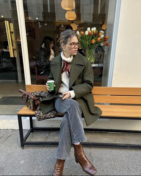 Parisian blond girl sitting on a bench with her coffee in hand. She is very in trend dressed. Her hair is up and is wearing brown squared glasses. She is wearing a thick white knitted turtleneck which she tied a thin elegant red satin  scarf around her neck. She associated this with grey jeans, brown leather block heels boots and a green jacket. Parisian Chic Style Fall, Paris Fall Outfits, Paris Winter Fashion, Green Jacket Outfit, Fall Jackets Outfit, Cardamom Buns, Khaki Coat, Christmas Instagram, Parisian Chic Style