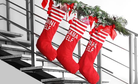 Three red Christmas stockings hang on a modern stair rail. Diy Stair Railing, Stocking Hangers, Stocking Hooks, Hanging Christmas Stockings, Christmas Stairs, Modern Stair Railing, Red Christmas Stockings, Stair Rail, Stocking Hanger