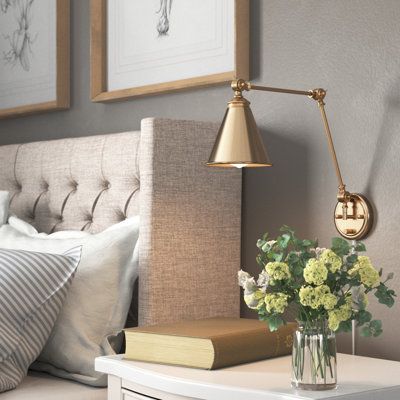 This 1-light wall sconce brings convenient light and classic style to any corner. It's made from metal with a neutral finish, and it has a cone-shaped steel shade for a vintage-inspired look. This sconce features a circular backplate with a slim linear arm that bends and turns to direct light exactly where you want it. The shade holds one standard bulb (sold separately). Whether you place this fixture in your entryway, hallway, or bedroom, it's sure to brighten your space. Finish: Gold | Three P Scones On Side Of Bed, Lights Over Headboard Above Bed, Picture Light Above Bed, Wall Mount Bedside Lamp, Wall Reading Lights Bedroom, Warm Bedroom Lighting Ideas, Over The Bed Lighting Ideas, Sconces Bedroom Master Suite, Bedside Lighting Wall Mounted