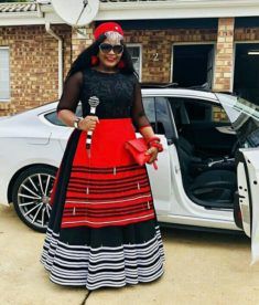 Beautiful Black Xhosa Umbhaco Dress With Red Apron, Red Beaded Cap and Beaded Stick Xhosa Attire For Ladies, Modern Xhosa Attire, South African Dresses, Xhosa Traditional Dresses, Xhosa Traditional Attire, Xhosa Attire, South African Traditional Dresses, African Traditional Wear, Traditional African Clothing