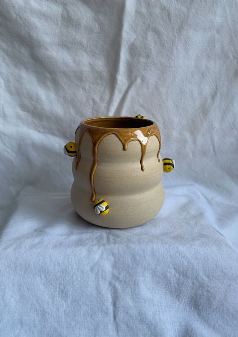 A unique, one of a kind pot handmade by me! This bumblebee pot is the perfect size for a small houseplant. The cute bees would be happy to look after whatever you choose to plant inside! How it's made: The shape is hand thrown on a pottery wheel, and the ceramic bees are hand crafted and painted before being attached to the main shape. I then use a golden yellow glaze and allow it to drip down the piece to mimic honey coming out of the bumblebee home. The piece is finally fired in a pottery kiln Ceramic Bees Pottery, Cute Ceramic Plant Pots, Cute Pottery Vase, Creative Pinch Pot Ideas, Honey Pot Pottery, Flower Pottery Ideas, Small Vase Pottery, Plant Pot Pottery Ideas, Highland Cow Pottery