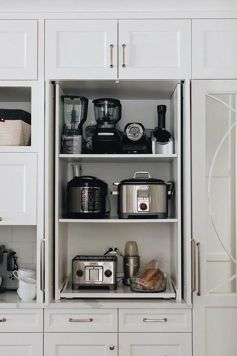 Fitted with pull out shelves, a small appliances cabinet is finished with white doors and nickel hardware and fixed beneath a white over head cabinet. Kitchen Appliances Cabinet, Cabinet With Pull Out Shelves, Appliances Cabinet, White Kitchen Shelves, Gorgeous White Kitchen, Kitchen Appliance Storage, Appliance Cabinet, تصميم داخلي فاخر, Pull Out Shelves